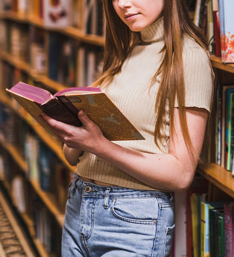 Emakume gaztea liburu bat irakurtzen liburutegi batean
